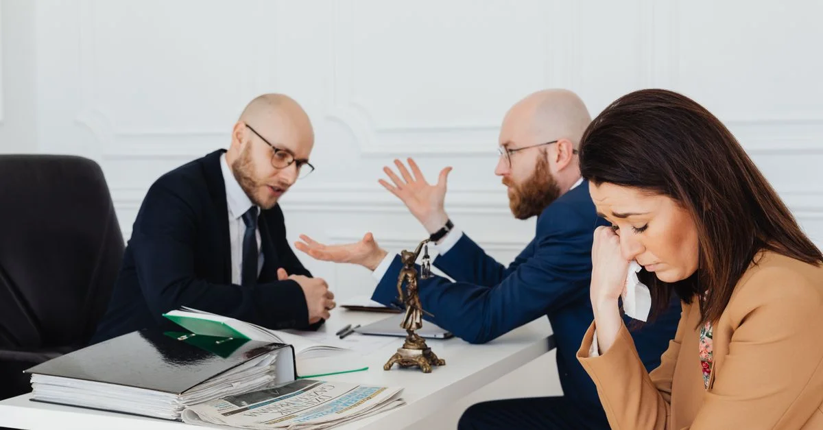 Une femme semble en détresse tandis que deux avocats conversent dans un bureau.