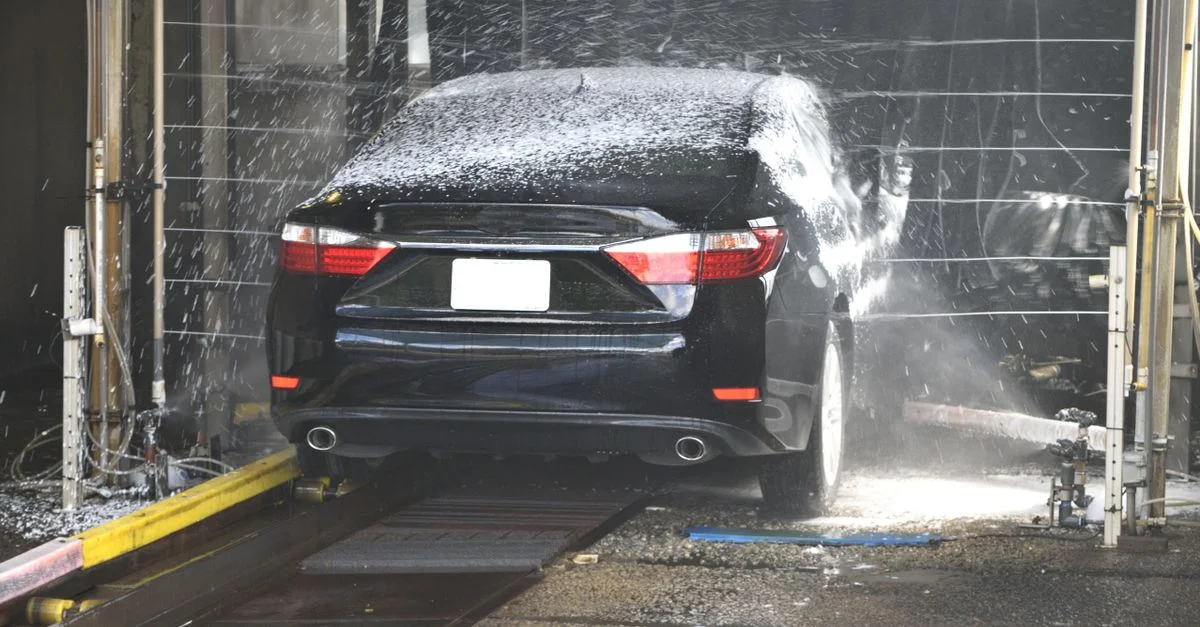 Une voiture noire nettoyée dans un lavage de voiture automatique avec de l'eau et de la mousse.