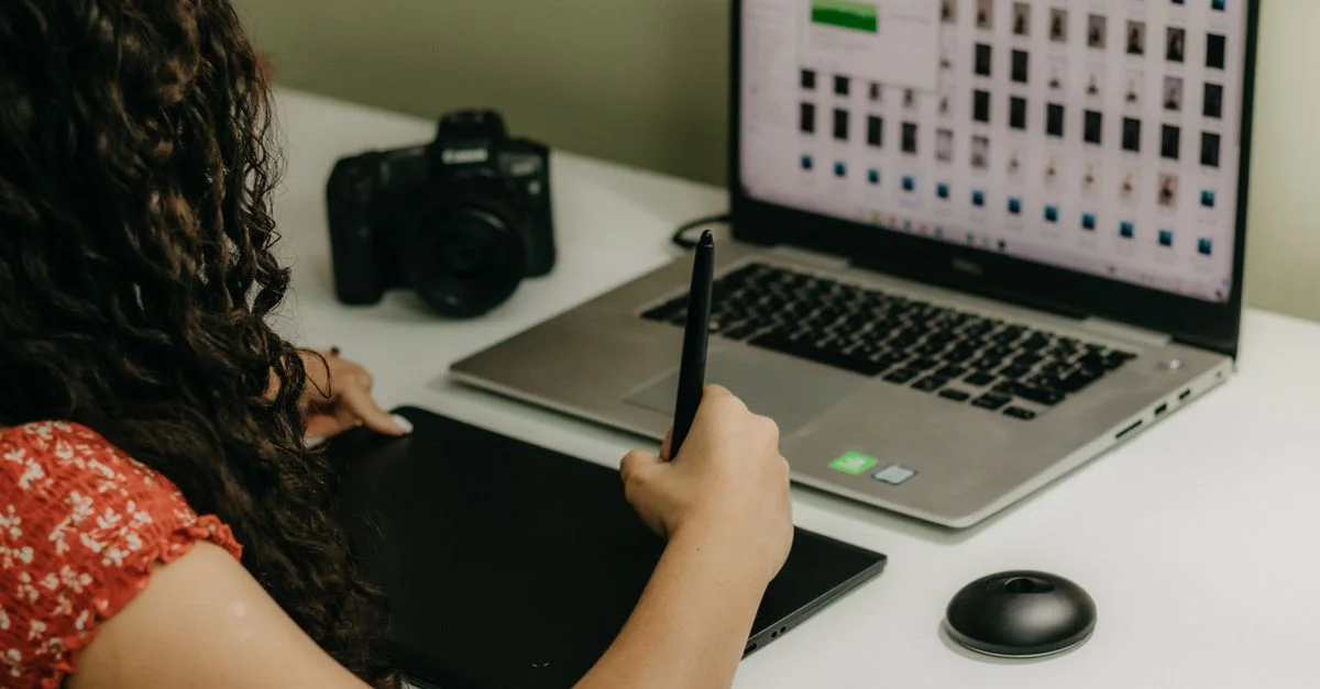 Femme utilisant une tablette graphique avec un ordinateur portable et une caméra dans un espace de travail créatif.