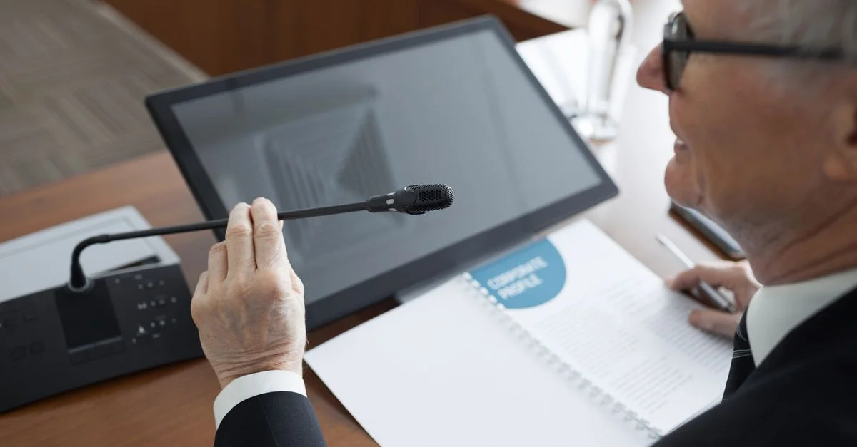 Un homme d'affaires senior utilisant un microphone lors d'une réunion de conférence avec des documents et un moniteur.