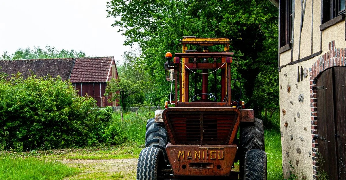 Un tracteur Manitou rustique garé près d'une ferme dans la campagne française, illustrant la vie rurale.