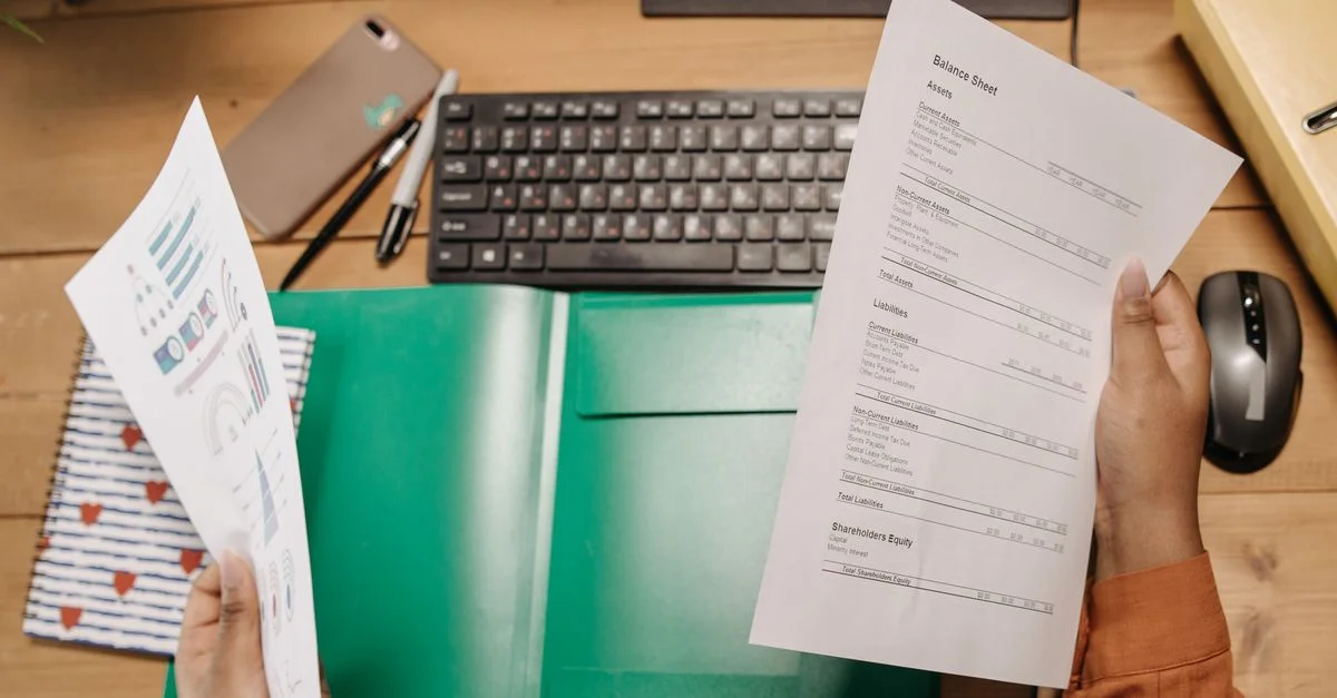 Mains tenant et examinant des bilans sur un bureau avec un clavier et des fournitures de bureau.