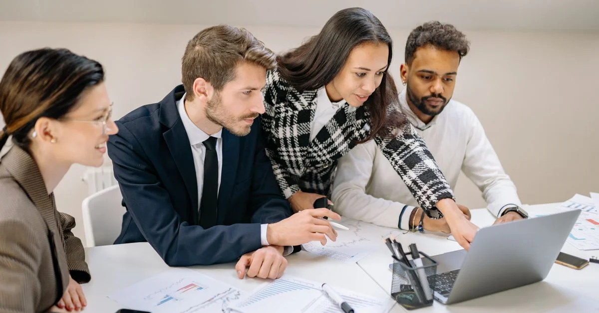 Équipe diversifiée de professionnels travaillant ensemble sur un laptop, analysant des graphiques et des données dans un cadre de bureau.