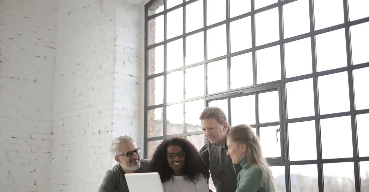 Groupe de collègues collaborant autour d'un ordinateur portable dans un espace de bureau moderne et lumineux.