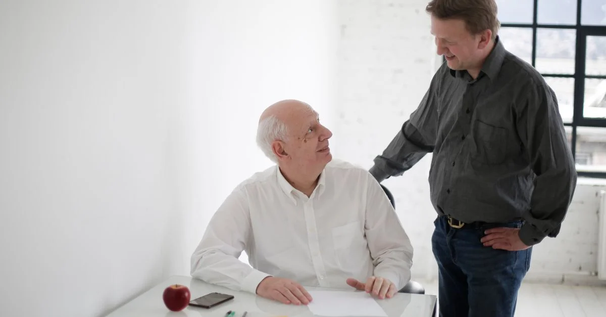 Deux hommes d'affaires ayant une discussion joyeuse tout en travaillant sur des documents dans un bureau moderne.