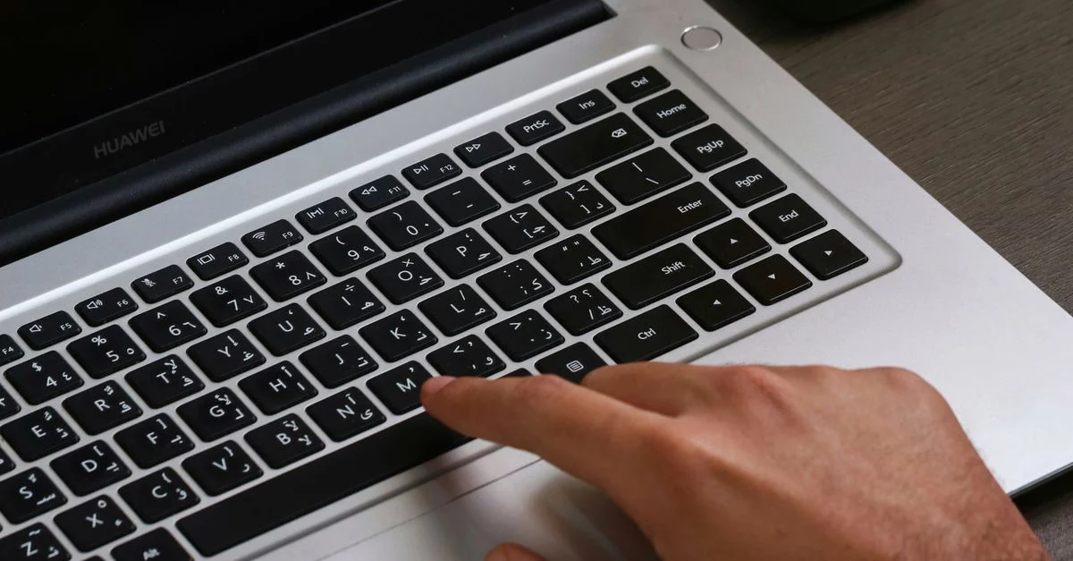 Doigts sur un clavier d'ordinateur portable avec du texte arabe, mettant en valeur la technologie moderne.