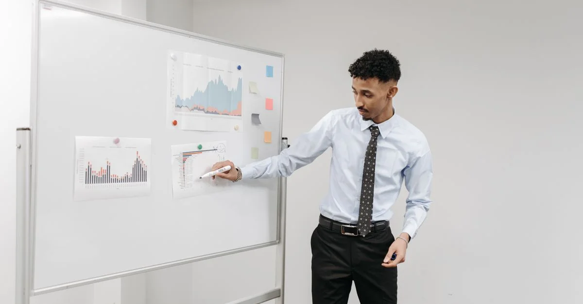 Homme présentant des graphiques sur un tableau blanc lors d'une réunion d'affaires dans un bureau contemporain.