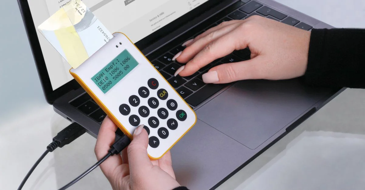 Gros plan sur des mains utilisant un lecteur de carte pour des transactions en ligne via un ordinateur portable, mettant en avant la technologie de paiement sans espèces.